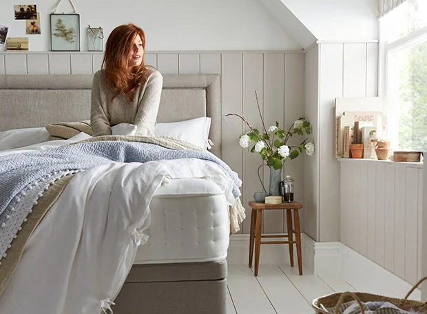 woman sat in light airy bedroom on semi-dressed bed