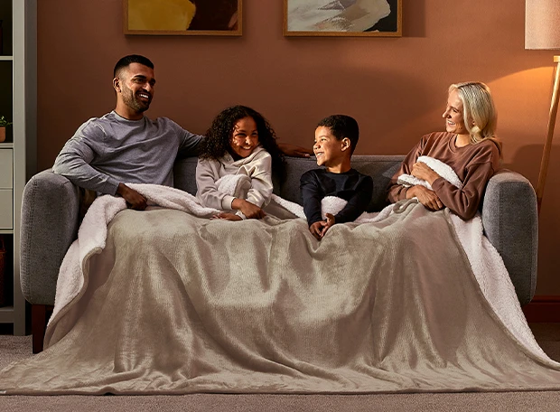 Family sat on a couch snuggled under a Silentnight Snugsie Giant Blanket