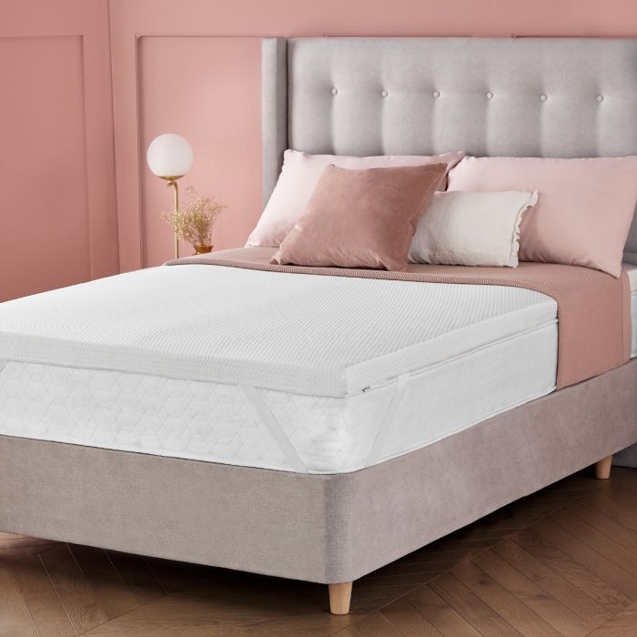 A grey bed in a pink room showing the Silentnight impress 5cm mattress topper 