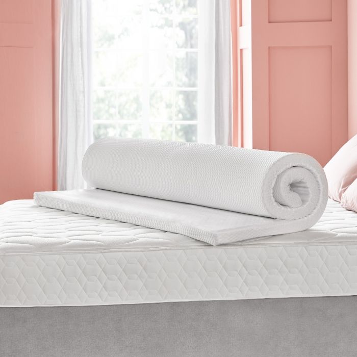 The Silentnight impress 5cm mattress topper rolled up on top of a bed in a pink room