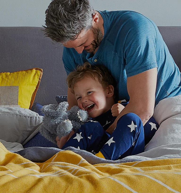 Man tickling child playfully on a bed