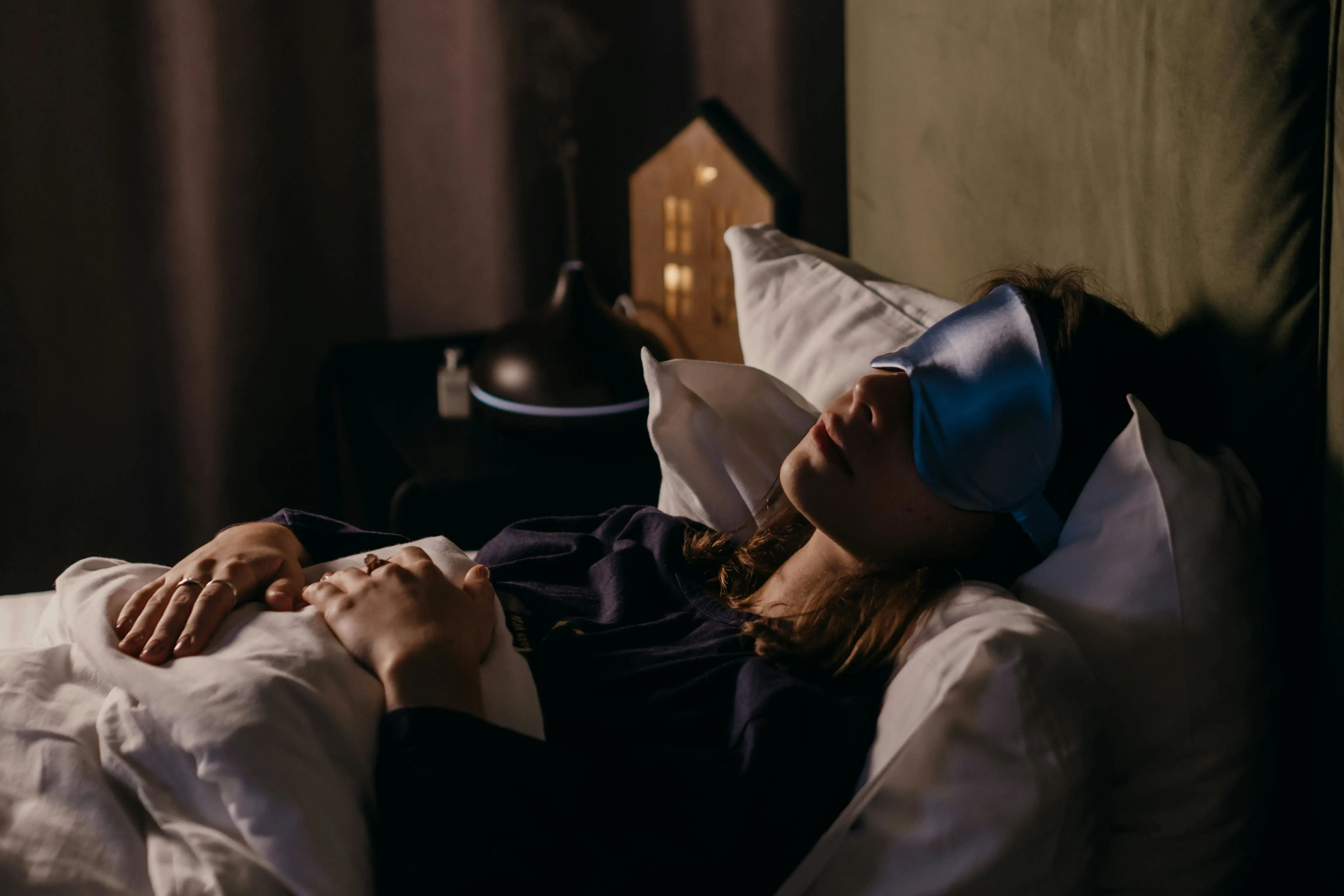 A lady sleeping wearing a silk eye mask in a dimly lit room.