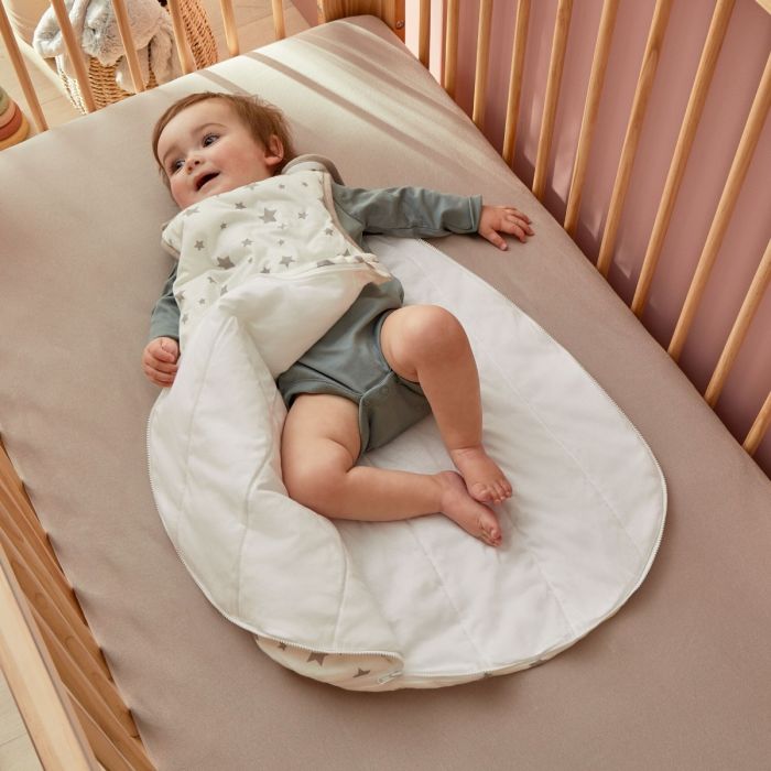 A happy baby lay in a cot wearing the Silentnight Safe Nights Stars Baby Sleep Bag with grey stars
