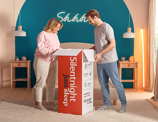A man and woman looking into an open box containing a rolled just sleep mattress