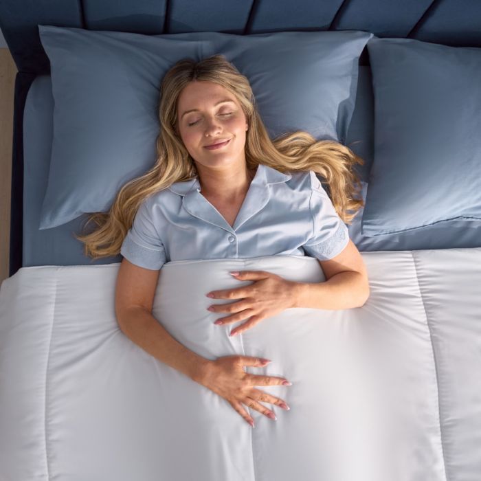 A person smiling in a blue bed whilst covered in the Silentnight Summer Breeze Duvet.